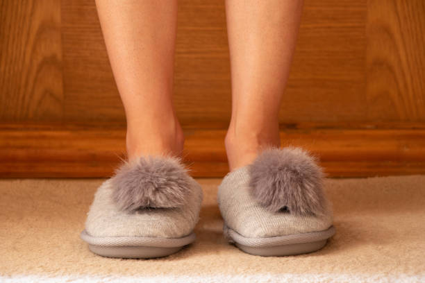 A girl in gray soft slippers with a bubo on the floor at home, home shoes, room slippers stock photo