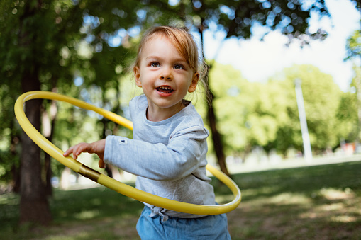 Cheerful smiling girl playing with hula hoop outdoors.