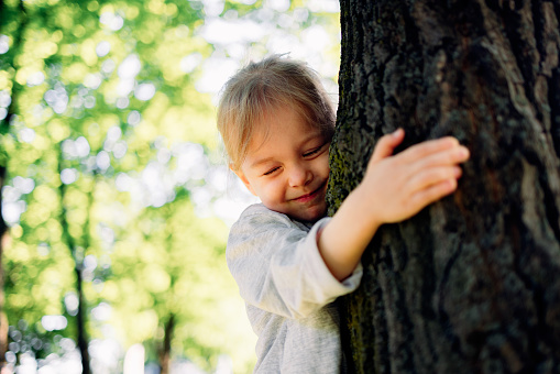 Low angle view of smiling girl embracing tree in the park.