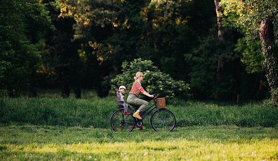 Side view of happy mother and her little girl having fun on a bicycle outdoors.