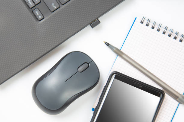 istock Computer wireless mouse, pen and notepad next to a laptop on a white table close-up. Items for office work 1413881162