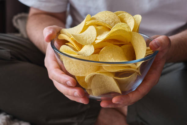 istock A man eats crispy potato chips from a transparent bowl on the couch. Quick snack. Calories and diet 1413881315