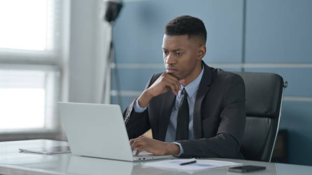 istock African Businessman Thinking while Working on Laptop in Office 1413882562