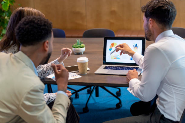 Financial services industry, Financial advisor or lawyer with couple explaining options. Financial advisor or lawyer with couple explaining options. They are discussing finance charts and graphs on a laptop computer. They sitting in an office and are discussing something with the agent Financial Planner Vs Financial Advisor stock pictures, royalty-free photos & images