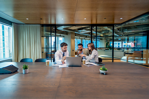 Business colleagues in a meeting, or Financial advisor or lawyer with couple explaining options. The agent is using a computer. All are well dressed. They sitting in an office meeting room. They are looking quite serious