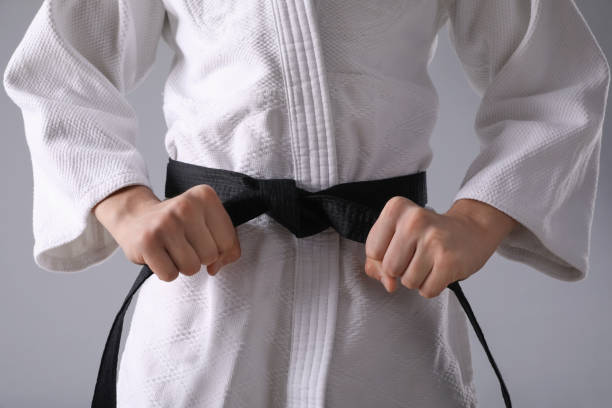 istock Martial arts master in keikogi with black belt on grey background, closeup 1413884937