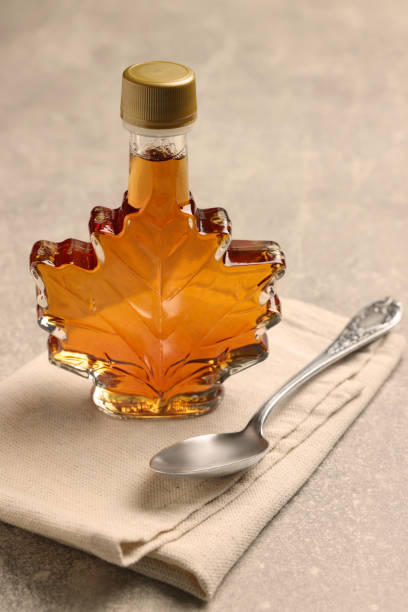 istock Leaf shaped bottle of tasty maple syrup and spoon on light grey table 1413885041