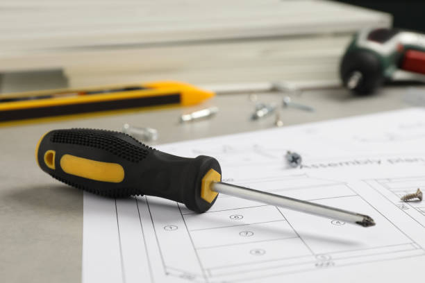 istock Furniture assembly plan, screwdriver and different fasteners on light grey table, closeup 1413885243