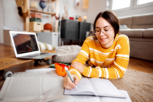 Young female student studying form home, while laying on the floor