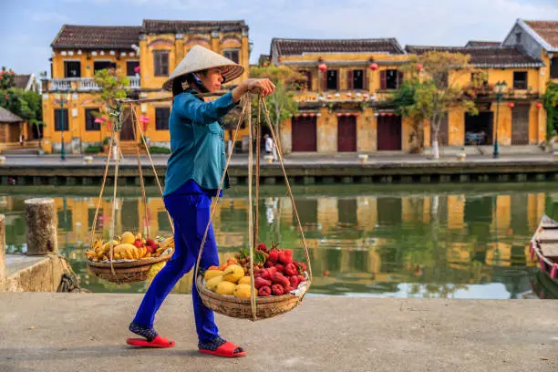 Vietnamese woman selling tropical fruits, old town in Hoi An city, Vietnam. Hoi An is situated on the east coast of Vietnam. Its old town is a UNESCO World Heritage Site because of its historical buildings.