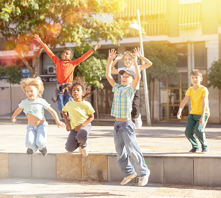 Group of cheerful children jumping on street at warm summer day