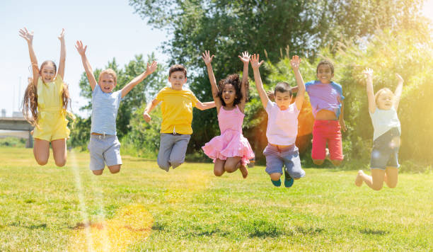 Schoolchildren  jumping and smiling together in park stock photo