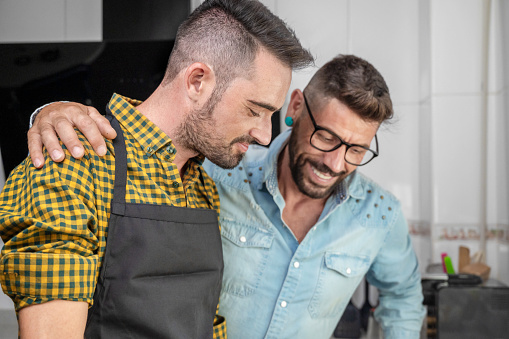 Happy hipster gay couple in love standing in the kitchen. They are cooking dinner together at home. High quality photography.