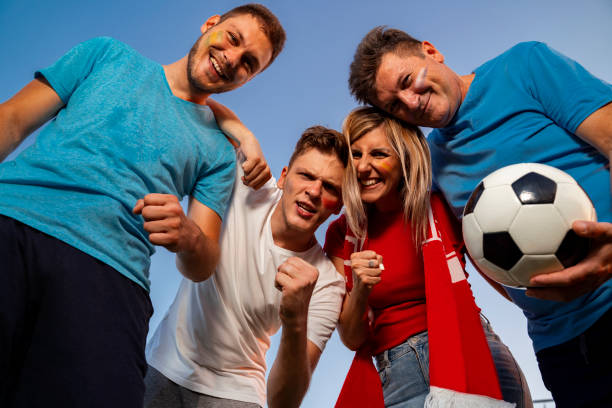 istock Group of ecstatic fans hugging together , view from bellow, sky background . Face paint on, fun mode on! 1413901030