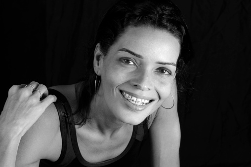 Studio Portrait in black and white of young woman in black t-shirt smiling at camera against black studio background. Salvador, Brazil.