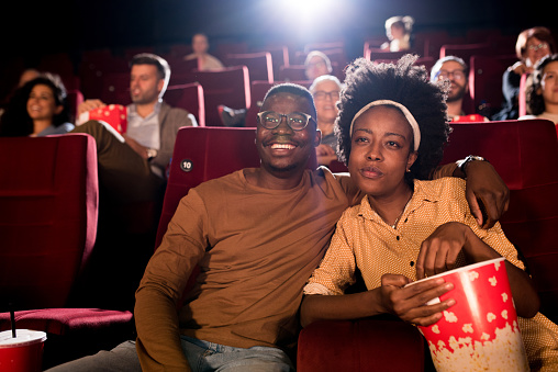 African-American couple watching a comedy movie at the cinema and enjoying.
