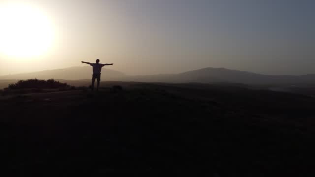 Silhouette of a man with arms raised on a hill and sunset.