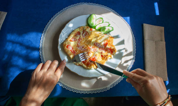 istock female hands cut scrambled eggs with tomatoes, on which the shadow from a curtain with tassels falls, breakfast on a sunny day 1413927048