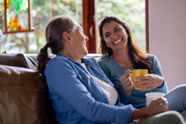 Happy mother and daughter laughing at home while drinking coffee
