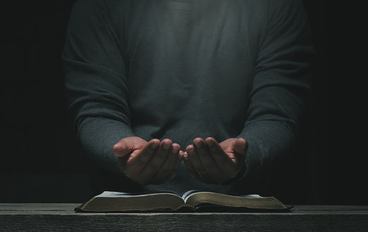 Men pray from god blessing to have a better life. Christian Crisis Prayer to God.  Men's hands praying to God with the Bible.  believe in good  Hold hands in prayer on a wooden table.