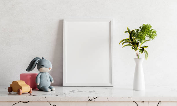 Empty photo frame mockup on white marble table with rabbit doll houseplant plant and wooden toy car. Art and interior home decoration concept. 3D illustration rendering stock photo
