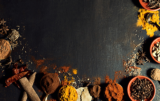 Spices, flavors and herbs on a black wooden table to prepare a tasty meal. Assortment or variety of Indian condiments to add to when cooking food. Seasoning scattered on a counter
