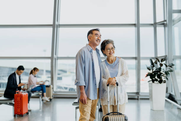 Smiling Asian senior couple tourists in airport Image of an Asian Chinese senior couple tourists in airport and ready to travel kuala lumpur airport stock pictures, royalty-free photos & images