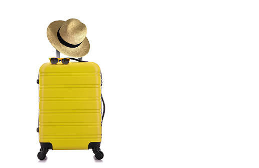 Travelling concept with yellow luggage with hat and yellow sun glasses isolated on white background