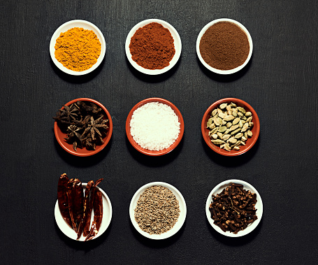 Assortment of Indian spices laid out in bowls on kitchen table. Cookbook showing vital ingredients to add to a native dish. Ingredients ready to be used by aspiring chefs in culinary school