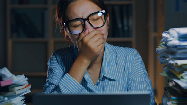 istock Overworked young Asian office employee yawn during working on laptop computer overtime at night in office 1413937734