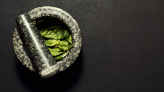 Cooking, preparing and making basil pesto with granite stone pestle and mortar against a black background with copy space. Above view of fresh, green and healthy herb leaves used in nutritious meals