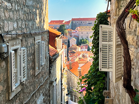 Glimpse of the Dubrovnik skyline and walls from the top of a steep street with stairs in Dubrovnik old town. Houses, windows and shutters.