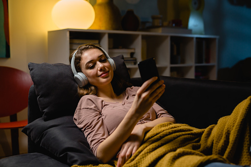 woman listening to a music and relaxing on sofa in her living room. night scene