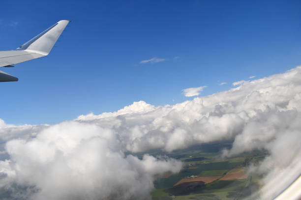 See-through airplane window with beautiful blue sky, white clouds floating above green farmland on the sunshine day.