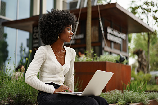 Young african american businesswoman working using laptop sitting on the bench in the city, close up