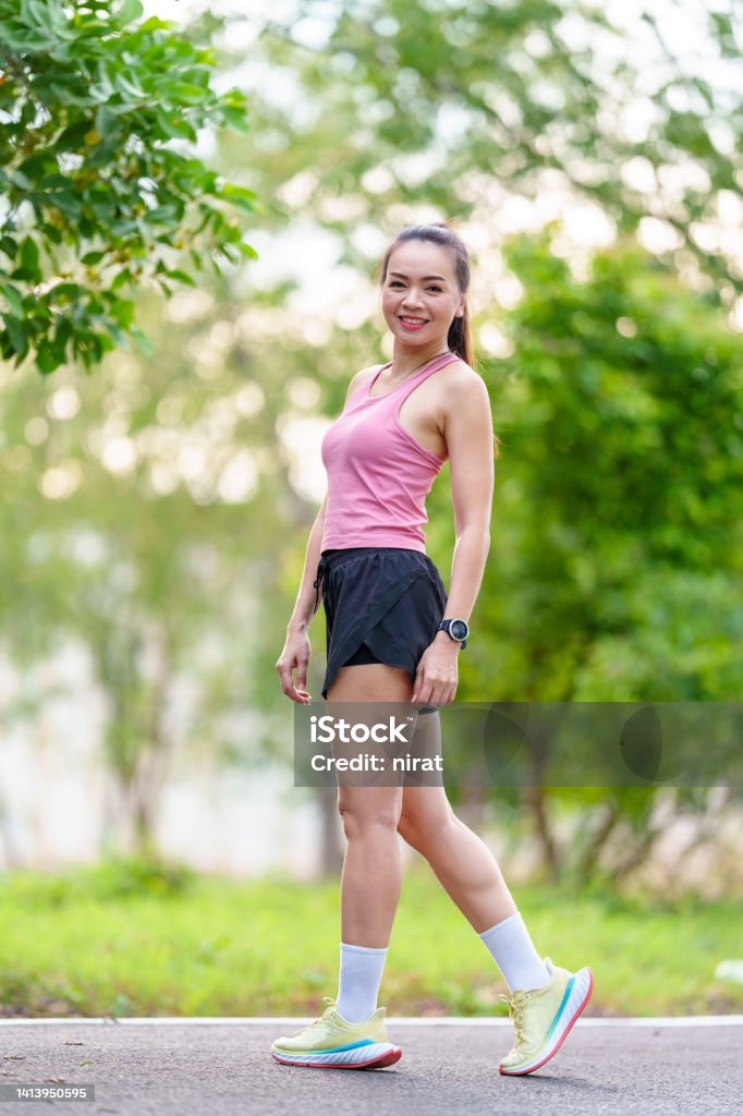 Portrait A cheerful Asian female runner in Outdoors outfits doing stretching before jogging exercise outdoor in the city natural park under healthy lifestyle concept Racewalking Stock Photo