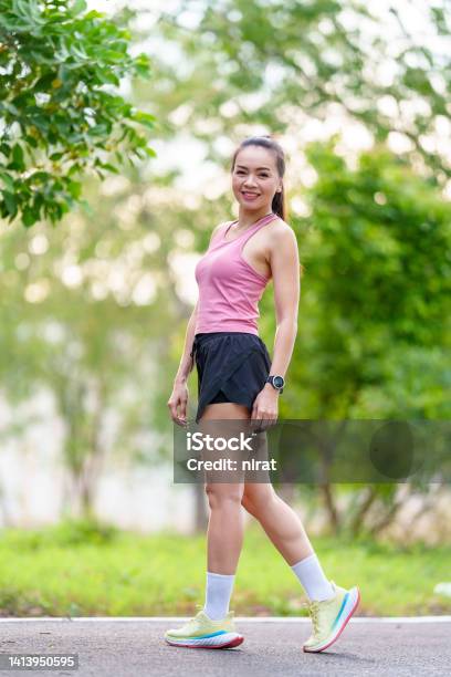 Portrait A Cheerful Asian Female Runner In Outdoors Outfits Doing Stretching Before Jogging Exercise Outdoor In The City Natural Park Under Healthy Lifestyle Concept Stock Photo - Download Image Now