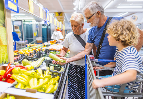 Photo of grandparents with one grandchild in the shopping. They are in supermarket buying groceries.Choosing vegetables..