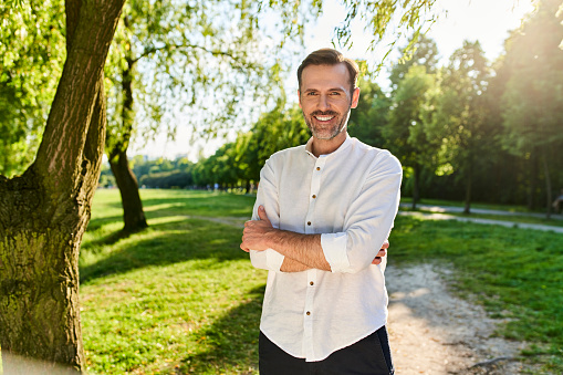 Portrait of smiling handsome man standing at park during summertime