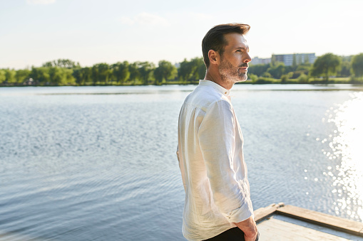 Portrait of a handsome man standing on a pier on a lake on a summer afternoon