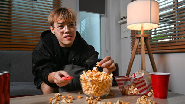 istock Man eating popcorn popcorn and watching TV at home. Leisure activity, relaxation, hobby concept. 1413957962
