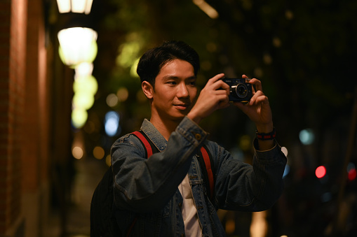 Man using smart phone while sitting on stairs in the night city with blurred night street lights background.