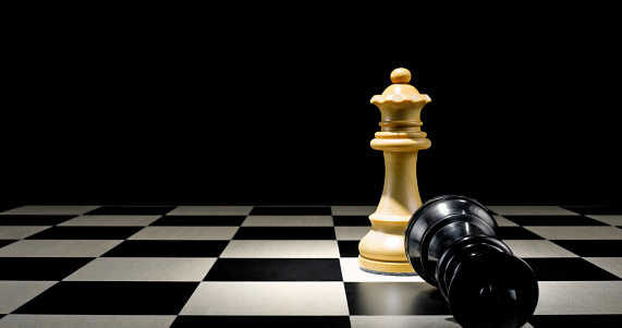 Close-up of king and bishop chess pieces on chessboard against black background.