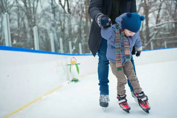 Photo of Father teaching his little boy to ice-skate outdoors in winter