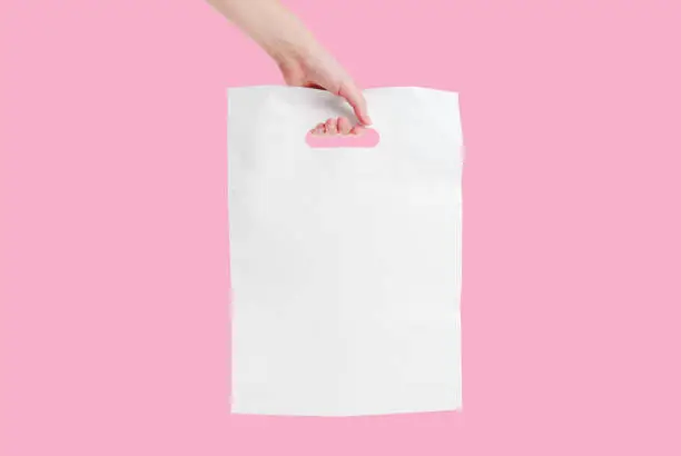 Plain white shopping bag in hand isolated on pink background. Boutique packaging.
