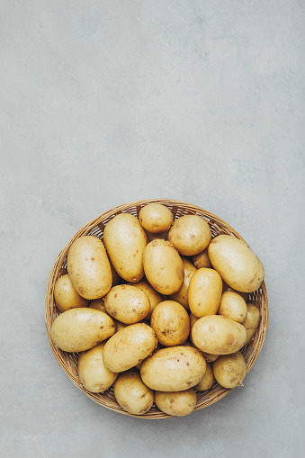 Potatoes. Bowl with young raw potato in bowl or basket  on grey stone background, top view with copy space