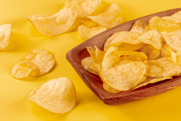 istock Potato chips or crisps in a bowl and scattered on a yellow background 1413972173