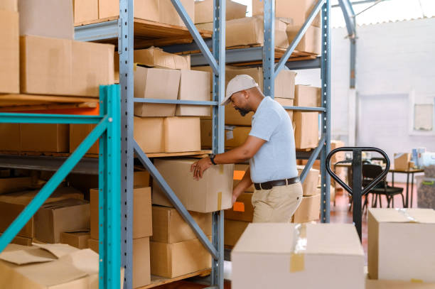 istock Warehouse, logistics and delivery man loading boxes on a cart or trolley for shipping in a factory. Inventory manager packing shelf or preparing parcels in a distribution center 1413972219