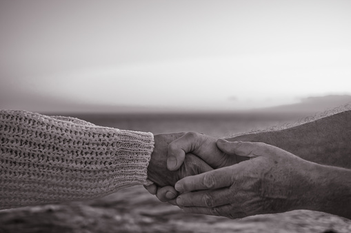 Black and white close-up of elderly man's hands holding elderly woman's hands