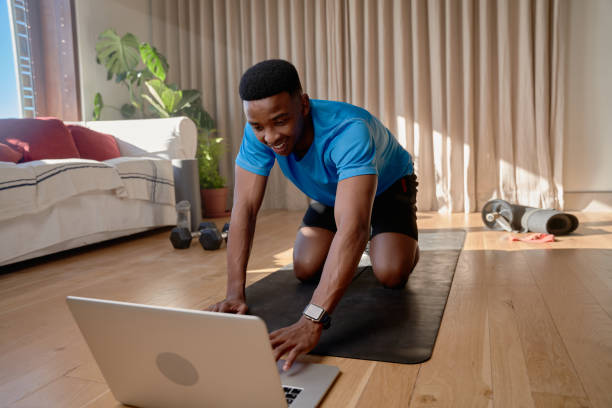 istock Young happy black African america male working out at home doing an online class using his laptop in his living room 1413973992